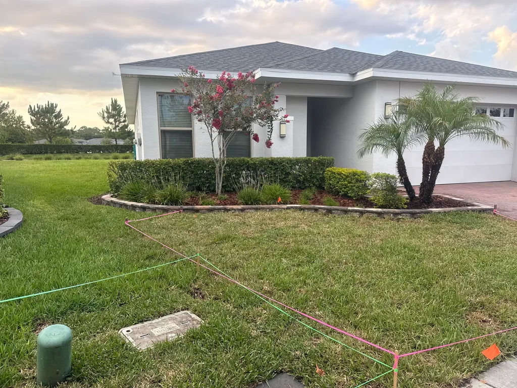 Planting bed with a flowering crape myrtle and a palm before a white stucco home
