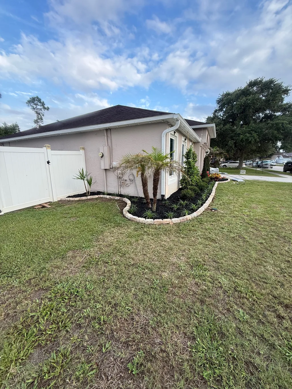 Curved tan block border wrapping a mulch bed with a small palm beside a mowed lawn