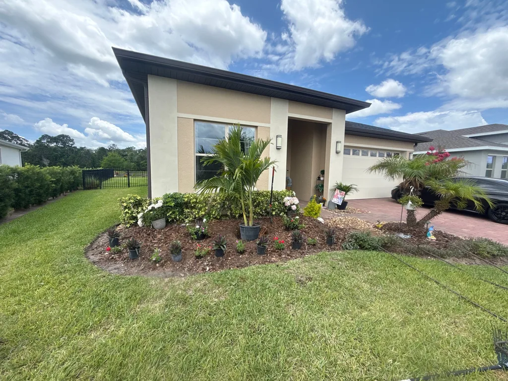 Finished front planting bed with palms and shrubs across the width of a stucco home