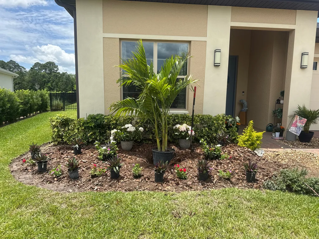 Flowering plants and palms arranged in a mulch bed along a cream stucco wall