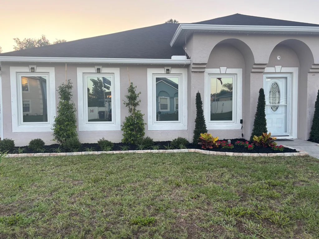 Trimmed shrubs and flowering plants in a bordered bed across a home front at dusk