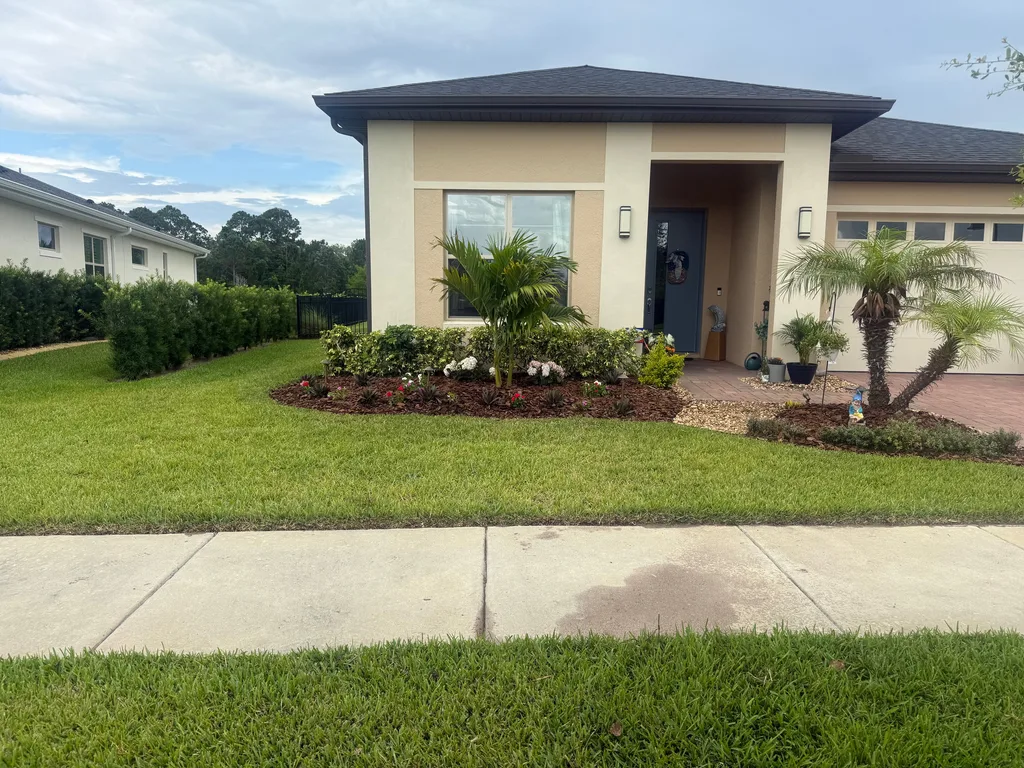 Curved planting bed with palms and low shrubs framing the entry of a tan stucco home