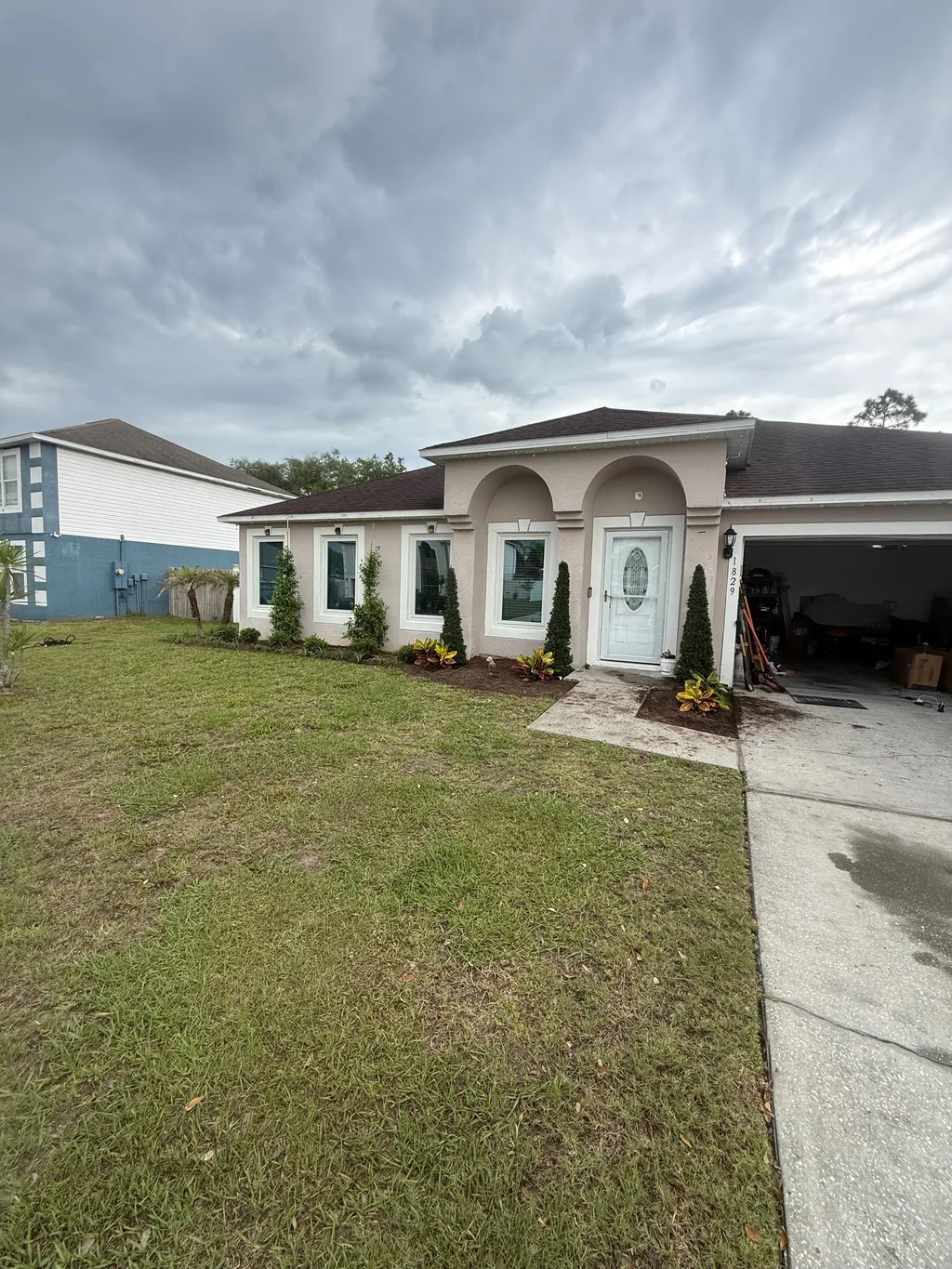 Upright shrubs and mulch beds running along the front windows of a stucco home