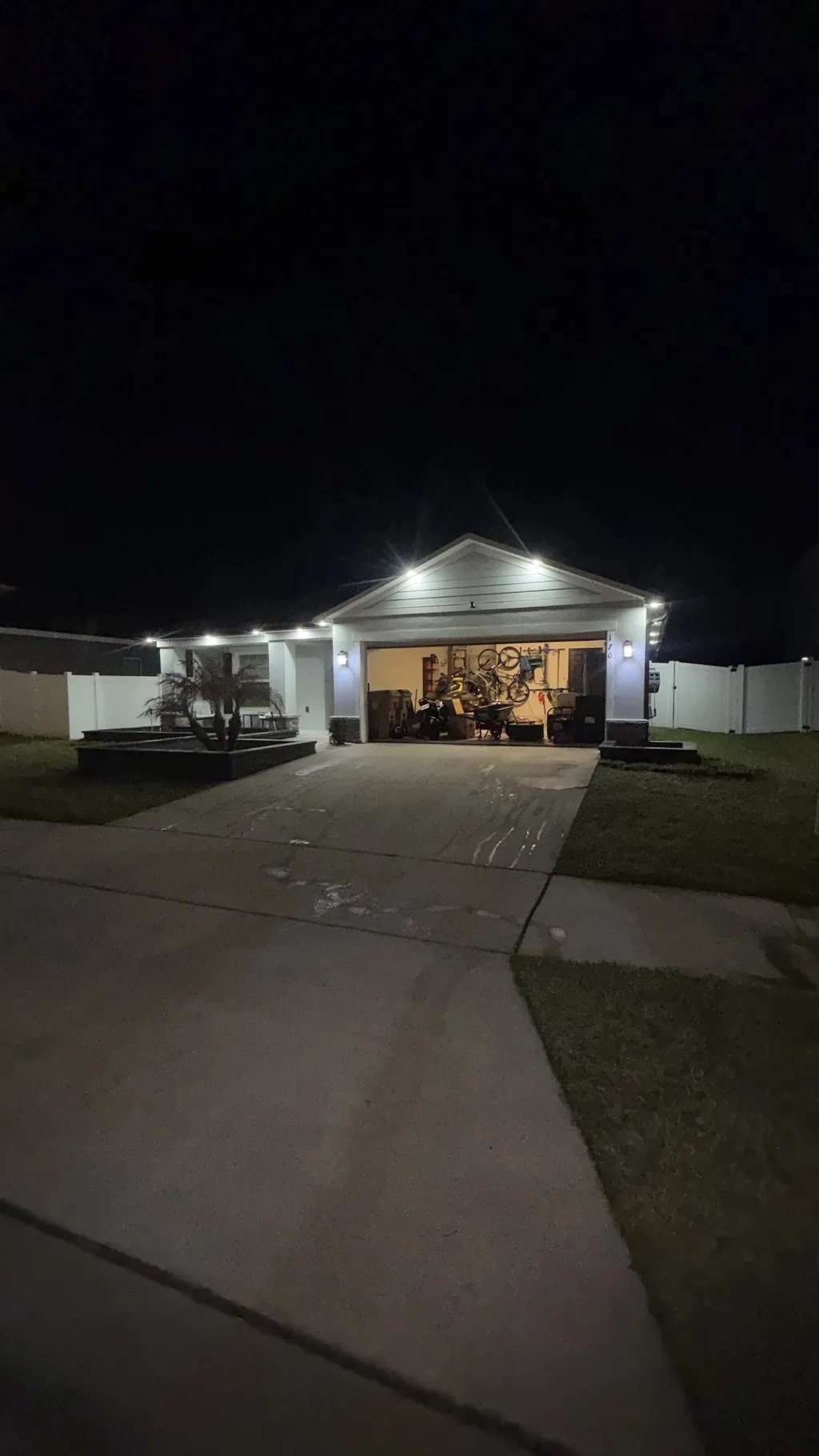 Home with exterior lights on at night above a wet driveway and an open garage