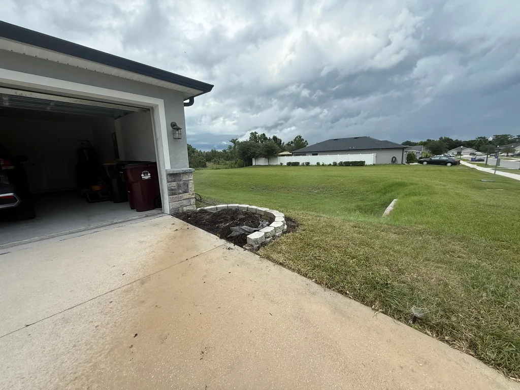 Mowed turf meeting a clean concrete driveway edge beside a stone trimmed garage
