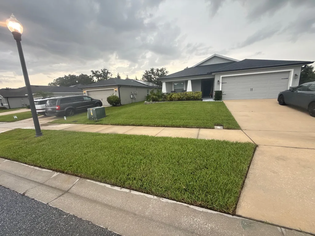 Evenly cut front lawn and driveway before a ranch style home in the evening