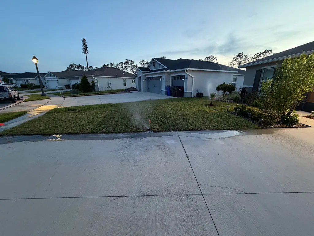 Wide mowed front lawn and concrete driveway at dusk as street lights come on