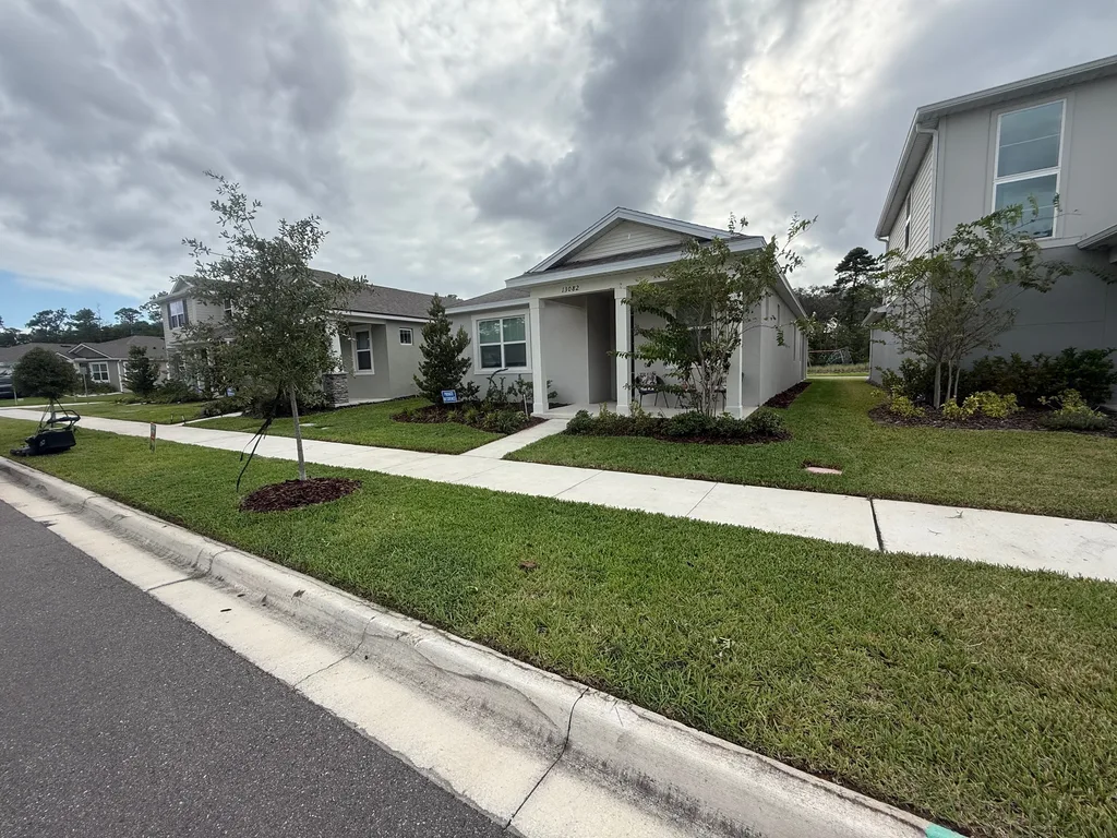 Mowed lawn and sidewalk in front of a newly built home with young trees