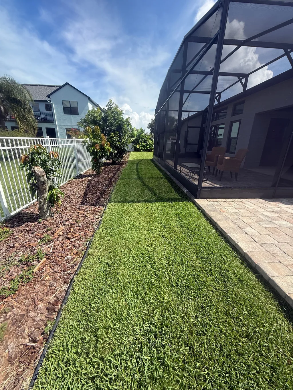 Mowed lawn running alongside a screened pool enclosure and a paver walkway