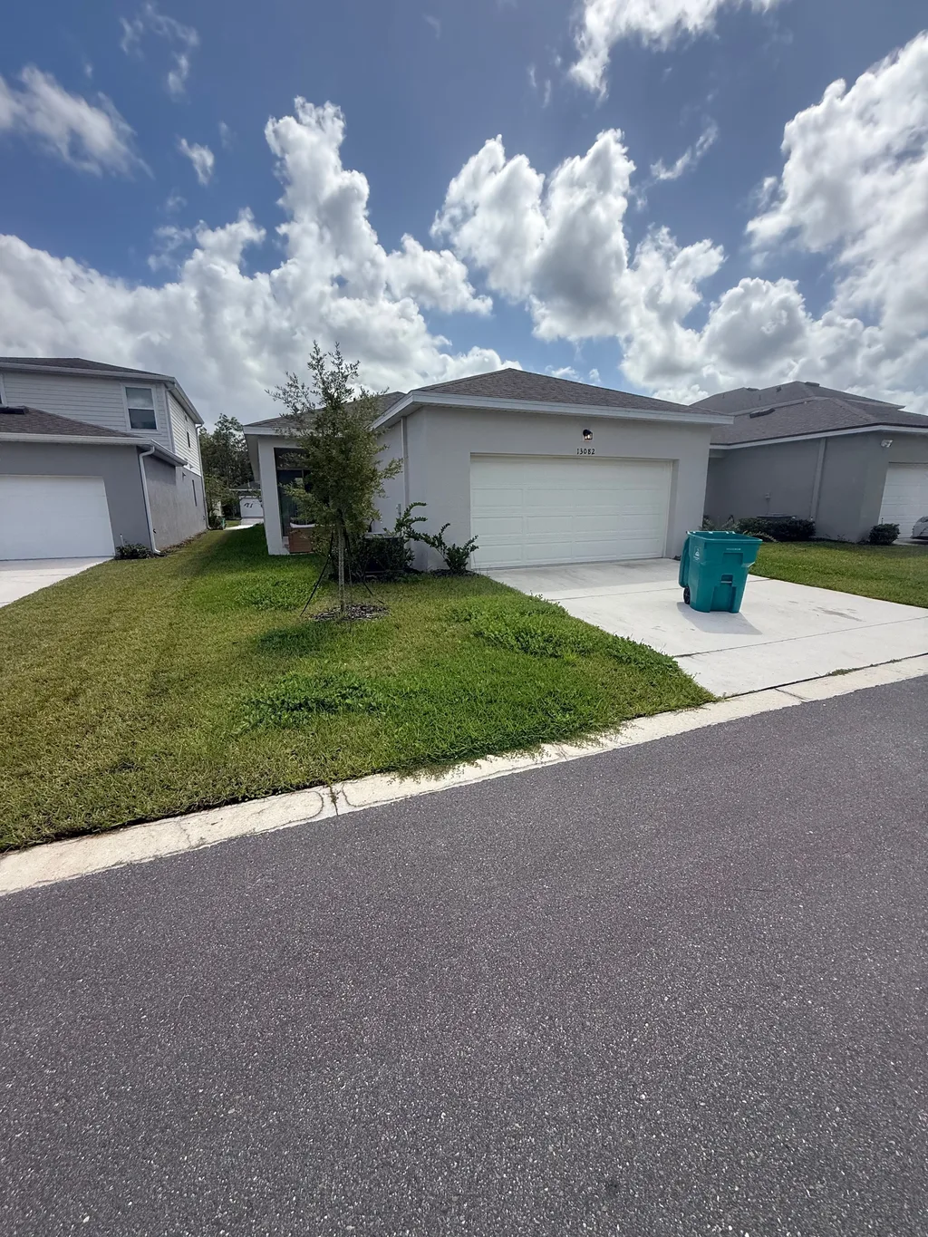 Cut lawn sloping to a driveway beside a two car garage and white trimmed home