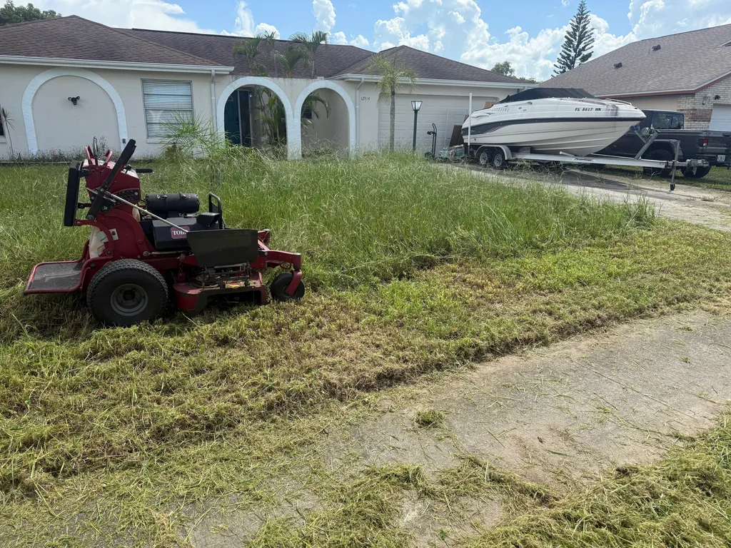 Zero turn mower cutting a sloped front lawn beside a paved residential driveway