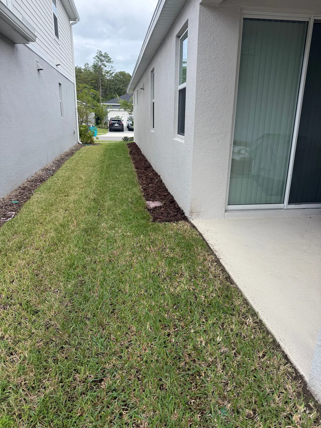 Narrow mowed strip of lawn running between a stucco wall and a neighboring property