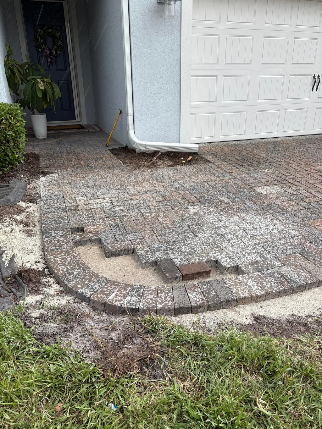 Curved paver apron being set into a sand base at the edge of a concrete driveway