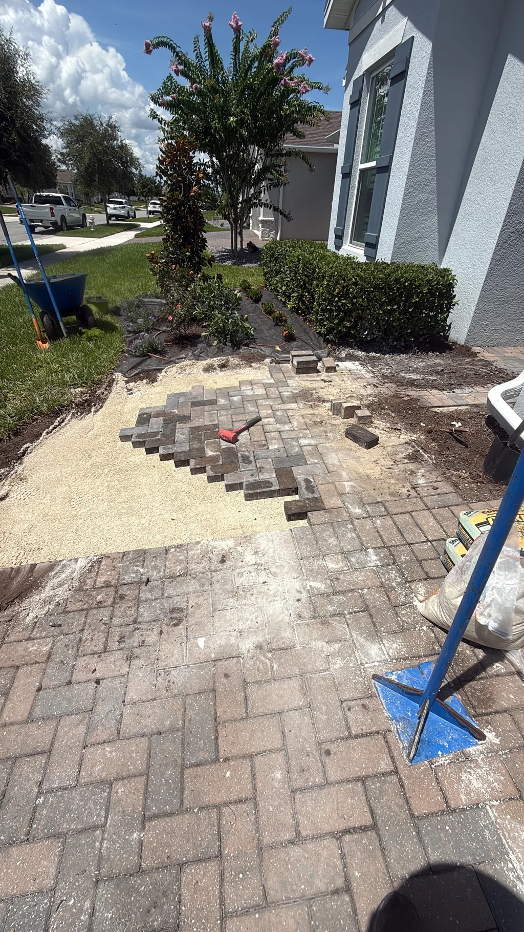 Pavers being laid in a running bond pattern over a compacted base beside a home