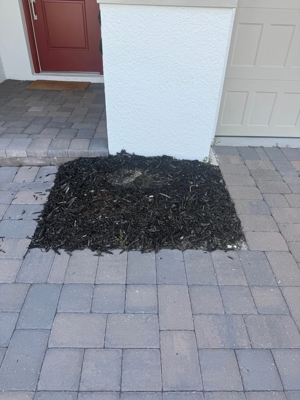 Large paver patio surface with a square mulch bed set into it beside a stucco wall
