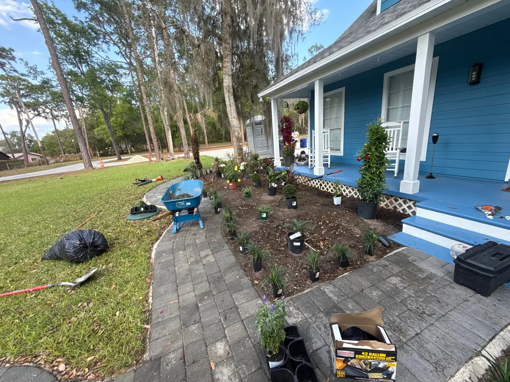 Paver walkway and planting bed under construction before a blue clapboard home