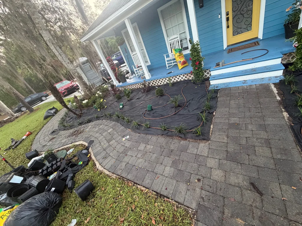 Curved paver walkway and planting bed being built in front of a blue painted home