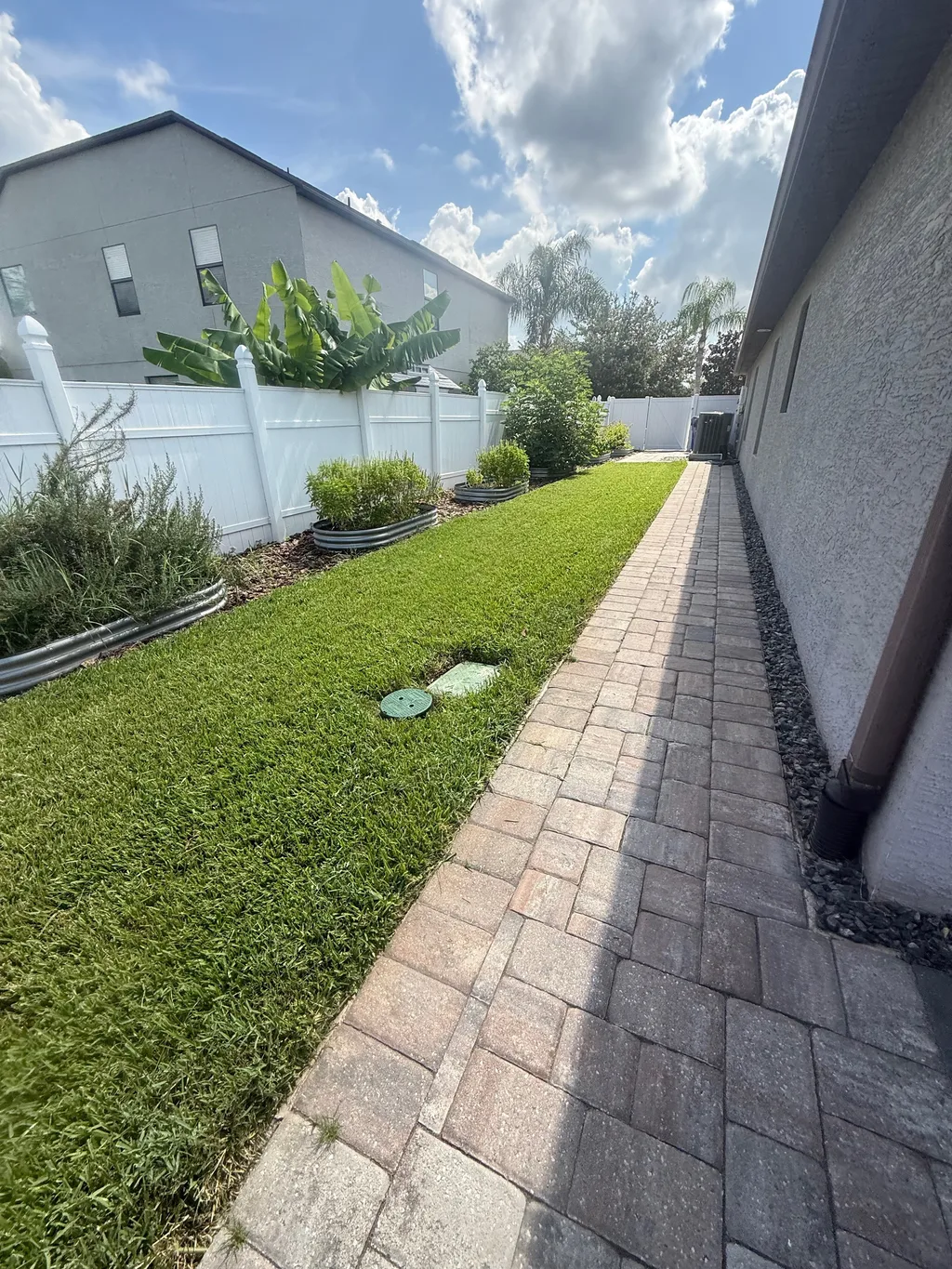 Paver walkway running a side yard between a stucco wall and a vinyl privacy fence
