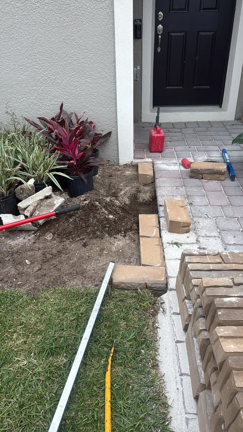 Paver walkway under construction with potted plants staged along the planting bed