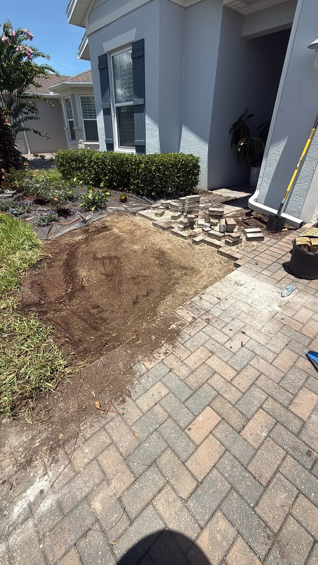 Paver walkway laid beside freshly turned soil and a trimmed hedge at a home entry