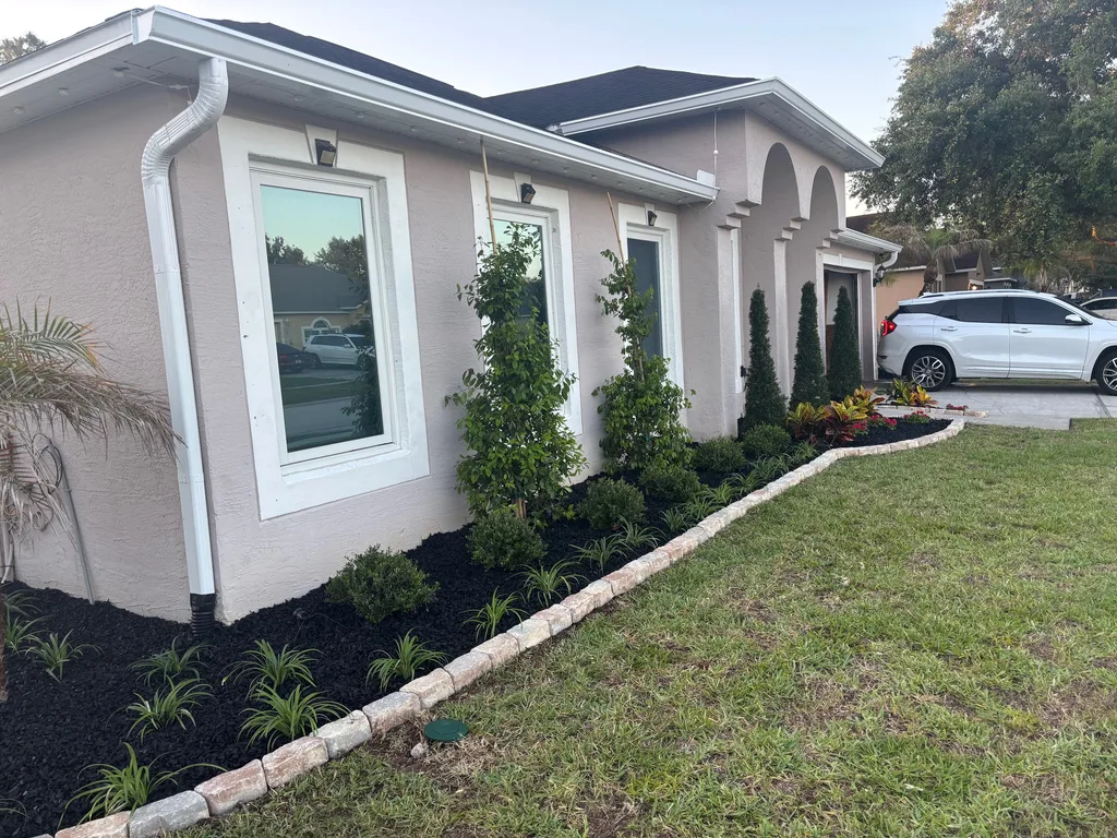 Young shrubs and ornamental plants in fresh mulch along the front of a stucco home
