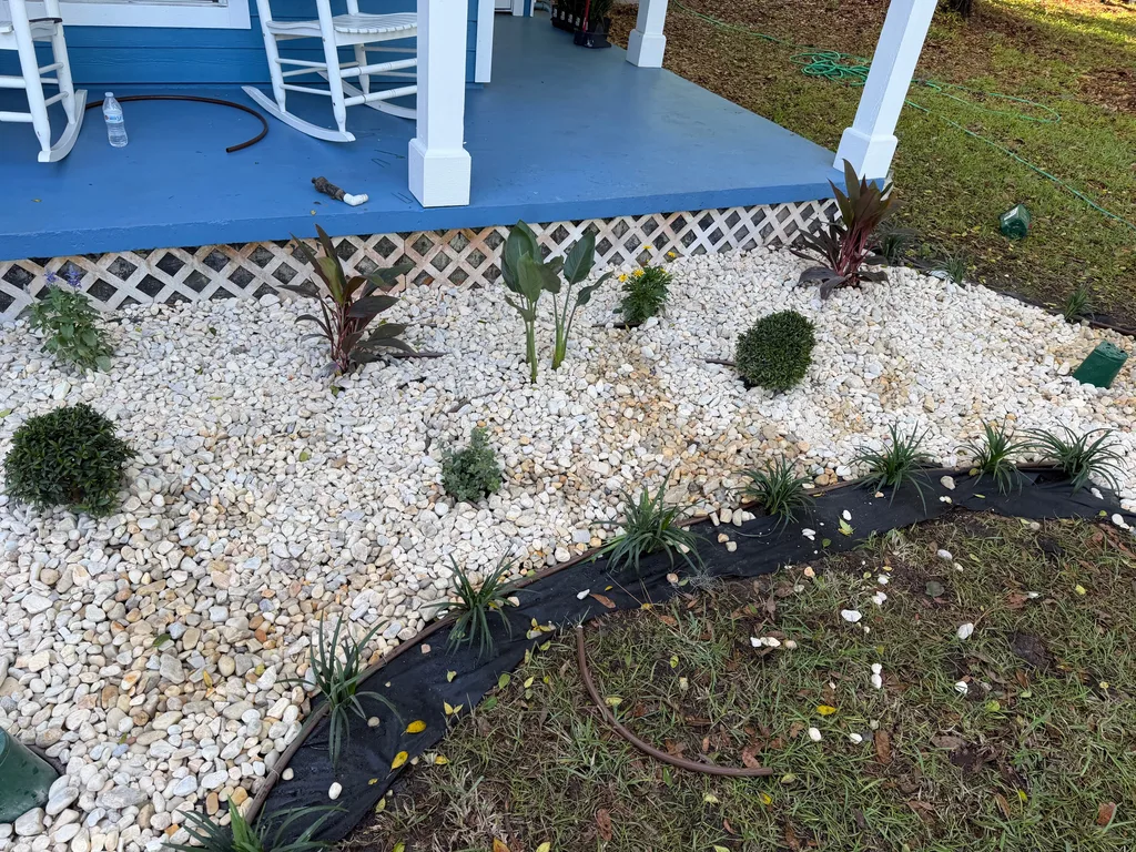 White decorative rock bed with young plants held by black edging beside a lawn