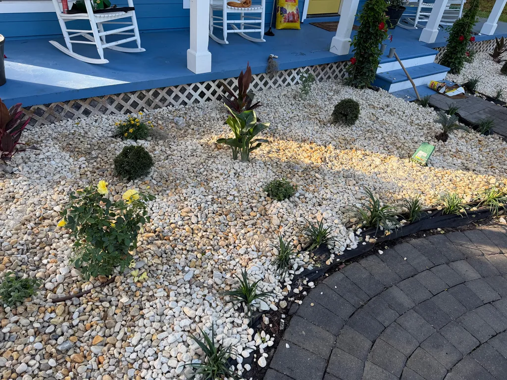 White decorative rock bed with small shrubs edged by a curved paver border